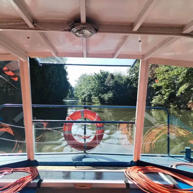Vue depuis l’intérieur d’un bateau naviguant sur la Deûle à Lille, encadrée par des berges verdoyantes sous un ciel dégagé.