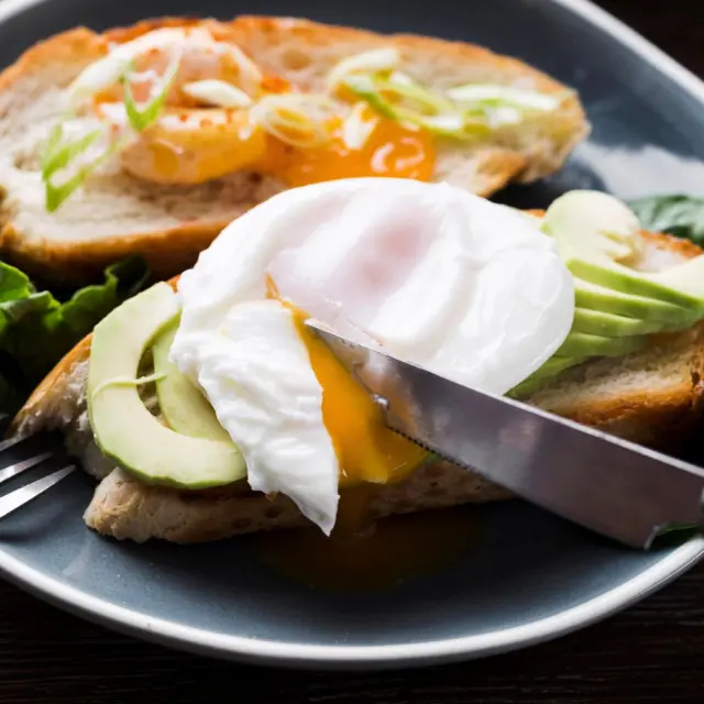 Œuf poché au jaune coulant servi sur une tartine à l’avocat, accompagné de jeunes pousses.