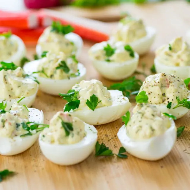 Œufs durs garnis de mayonnaise aux herbes et parsemés de persil frais sur une planche en bois.