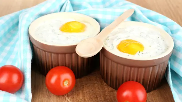 Deux œufs cocotte servis dans des ramequins avec une préparation crémeuse aux herbes, accompagnés de tomates.