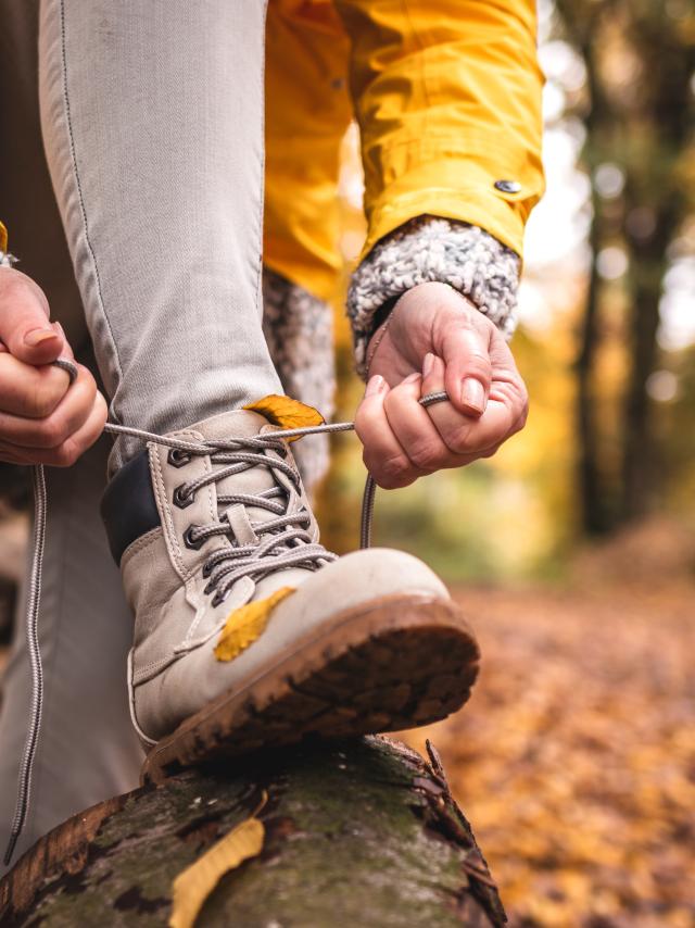 Woman tying shoelace on her hiking boot. Tourist is getting ready for autumn hike at woodland trekking trail
