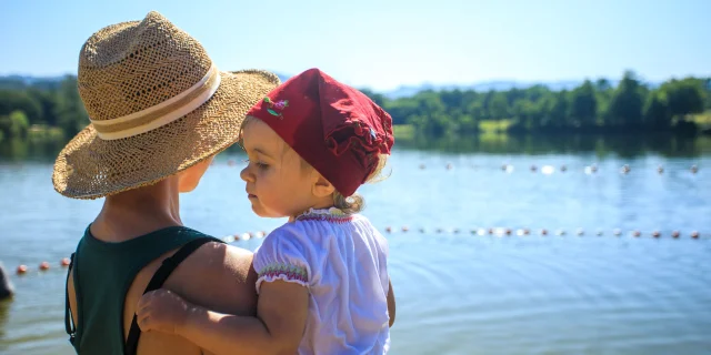 Une mère portant son enfant dans les bras contemple le plan d’eau Iloa à Thiers, par une belle journée d’été en Auvergne-Rhône-Alpes.