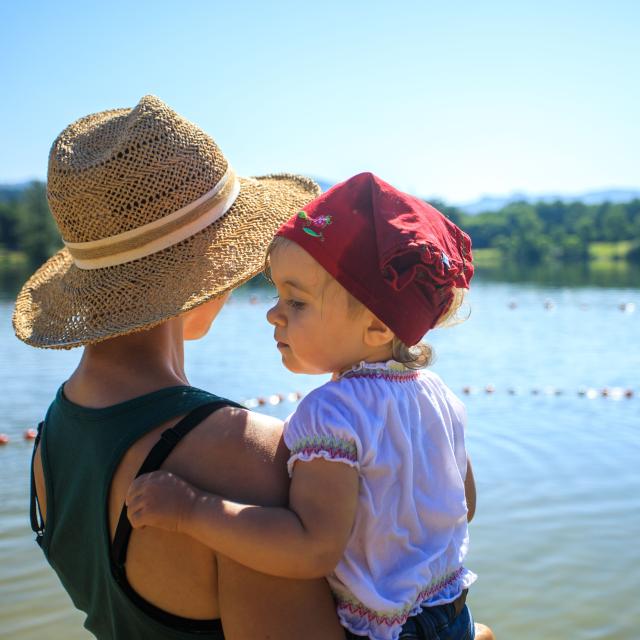 Une mère portant son enfant dans les bras contemple le plan d’eau Iloa à Thiers, par une belle journée d’été en Auvergne-Rhône-Alpes.