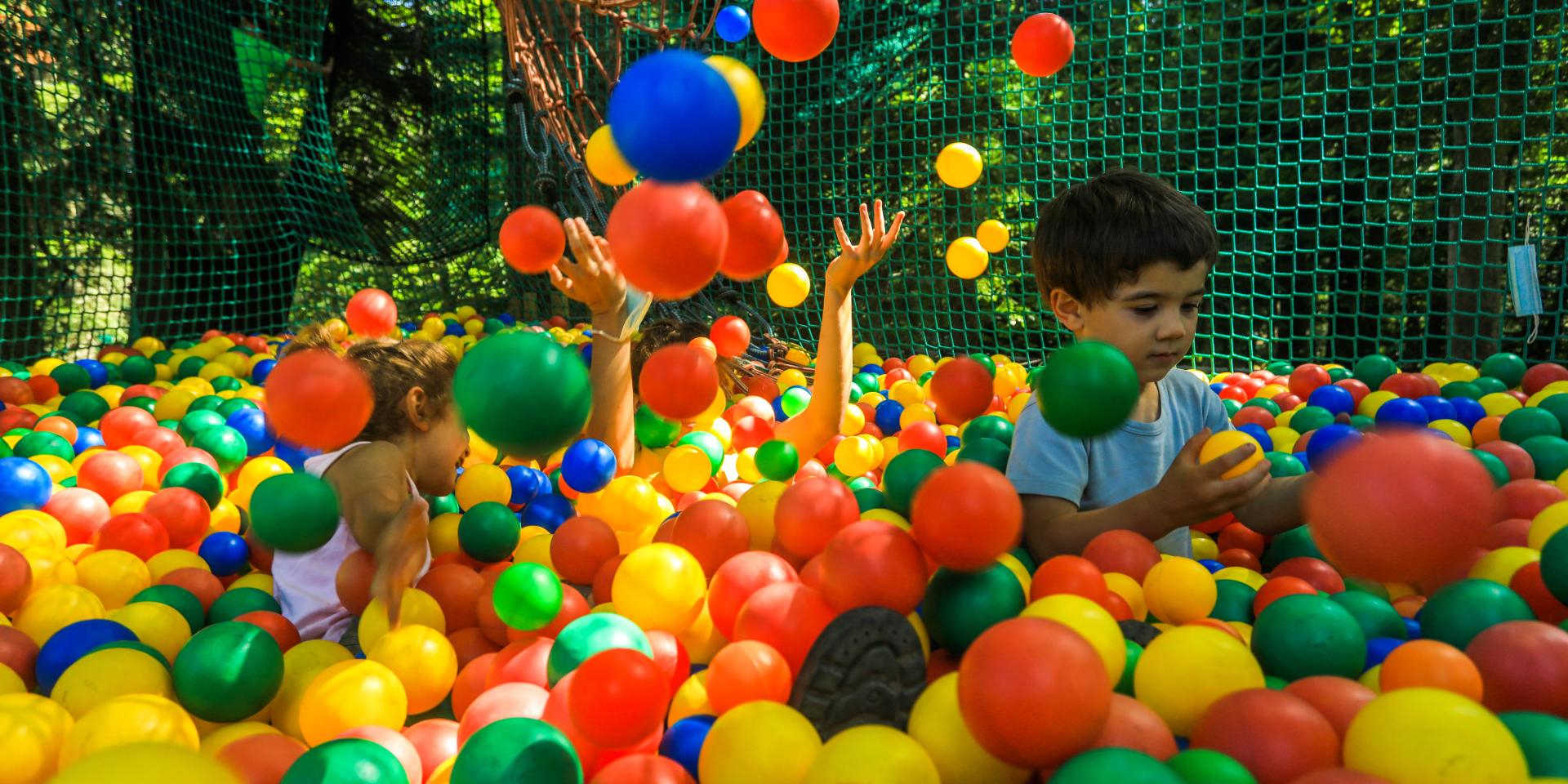 Trois enfants jouent dans un filet à Prabouré, entourés de boules colorées, avec des arbres en arrière-plan.