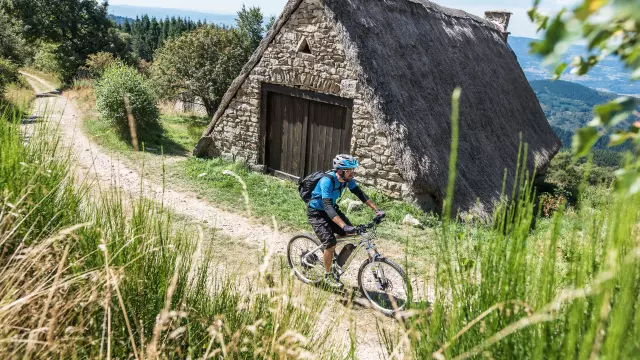 Cycliste en VTT devant une jasserie sur les crêtes du Forez, entouré de végétation et d’un paysage dégagé.