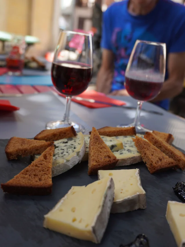 Plateau de fromages locaux avec du pain grillé et deux verres de vin rouge sur le marché d’Ambert.