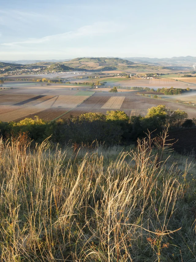 Vue panoramique de Seychalles, avec champs, collines et montagnes en arrière-plan.