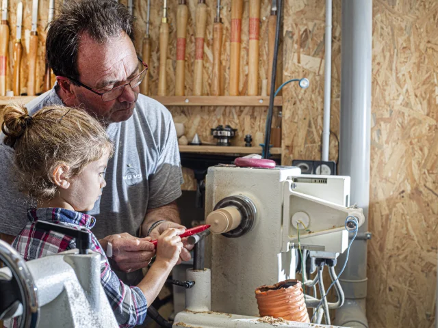 Un artisan du Cœur de Bois à Thiers explique les techniques de travail du bois à une petite fille, tout en lui présentant l’une des machines utilisées dans la fabrication artisanale