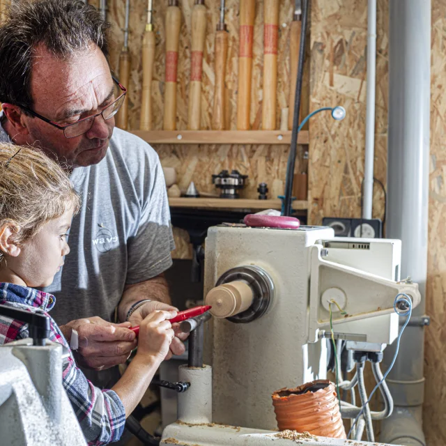 Un artisan du Cœur de Bois à Thiers explique les techniques de travail du bois à une petite fille, tout en lui présentant l’une des machines utilisées dans la fabrication artisanale