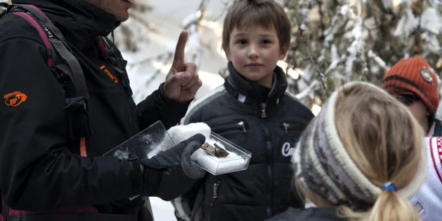 Visite guidée dans un paysage enneigé, un guide explique des sujets naturels aux enfants, tous bien habillés pour l'hiver.