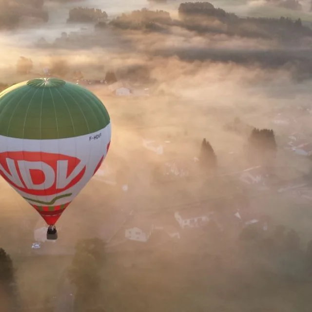 Montgolfière au-dessus d’un paysage de brume à Viverols, dans la Vallée de l'Ance, avec des habitations visibles.