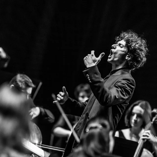 Chanteur en pleine prestation, entouré de musiciens, lors du Festival Arioso – Nuits Classiques de Thiers, image en noir et blanc.