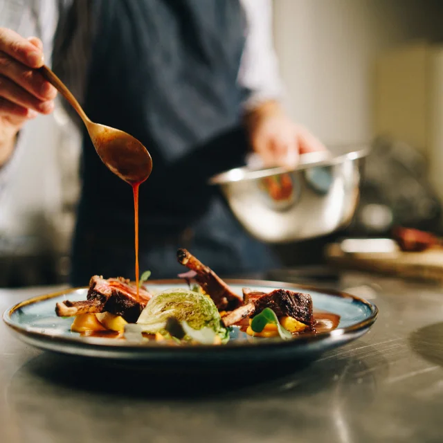 The chef pouring special sauce on pork ribs in the kitchen