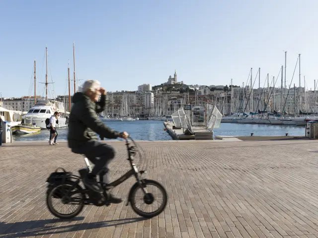 promeneur à vélo sur le Vieux-Port, en fond Notre-Dame de la Garde