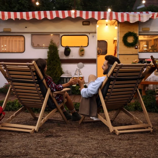 Young couple toasting with bottles of beer near trailer. Camping season