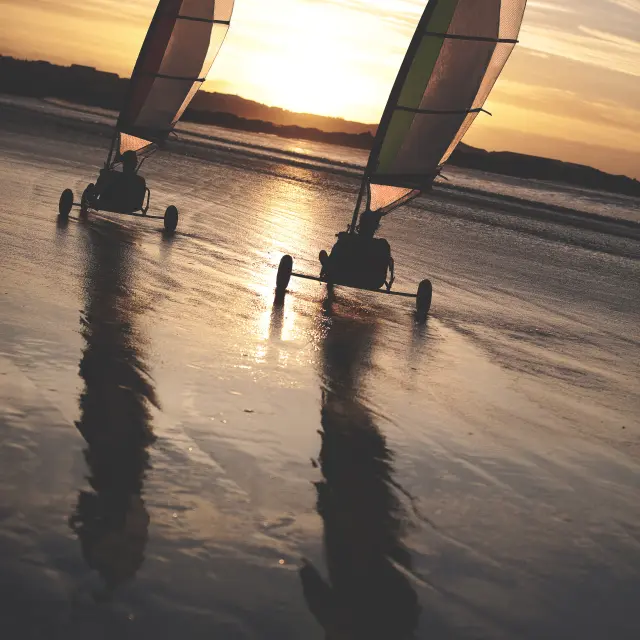 Dos veleros de arena compitiendo por una playa de arena al atardecer.