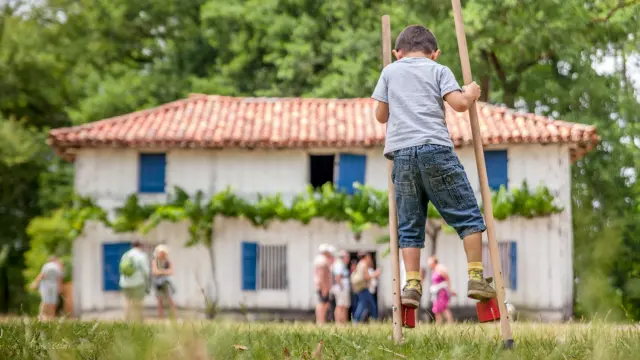 Échassier devant une maison traditionnelle à l’Écomusée de Marquèze