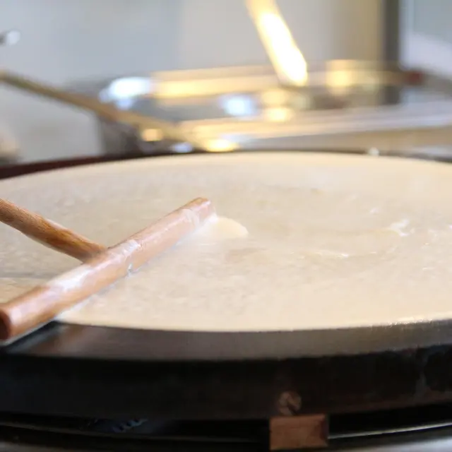 Étalement de la pâte à galette sur un billig traditionnel à l'aide d'un rozell en bois