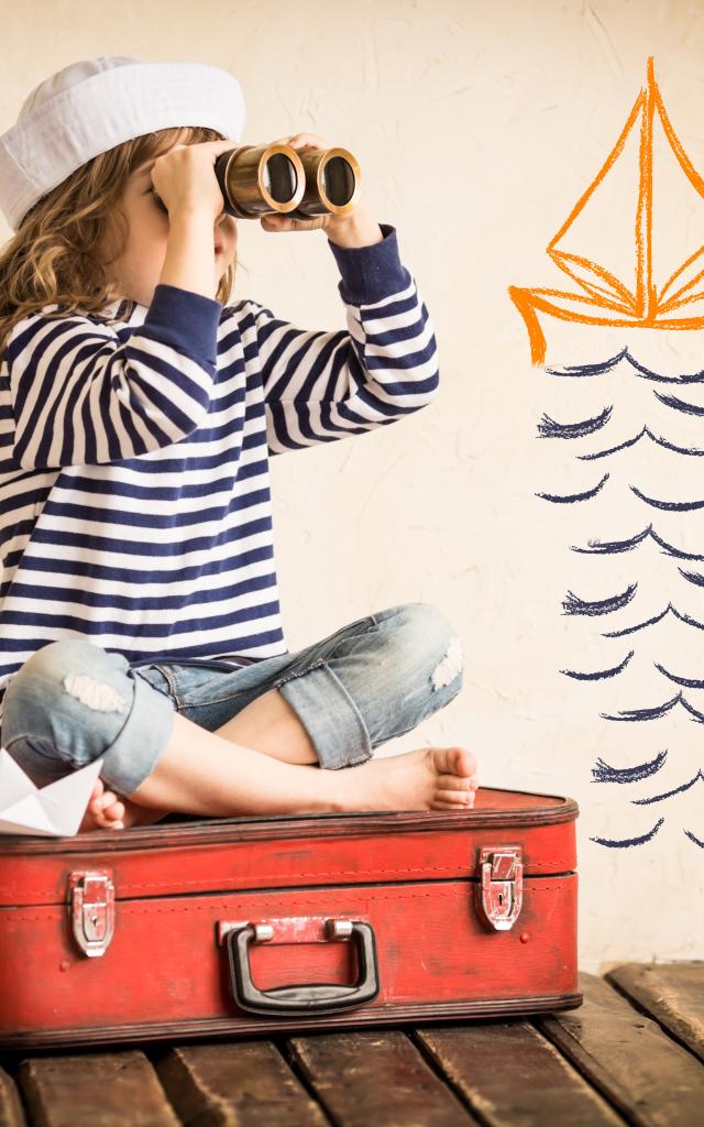 Happy kid playing with toy sailing boat indoors. Travel and adventure concept