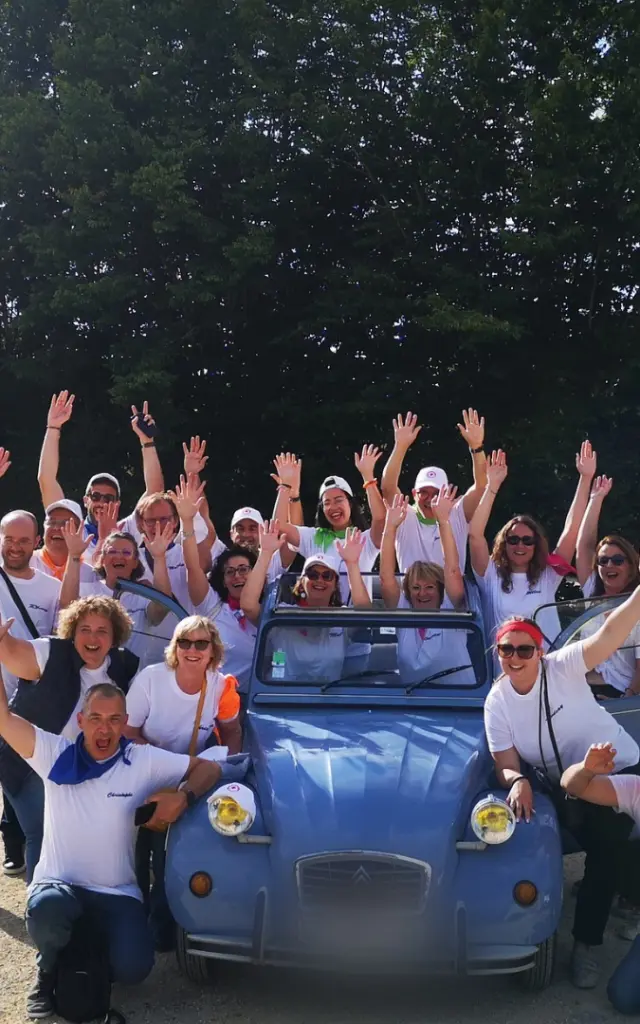 Une grande équipe de professionnels pose joyeusement autour d'une Citroën 2CV bleue