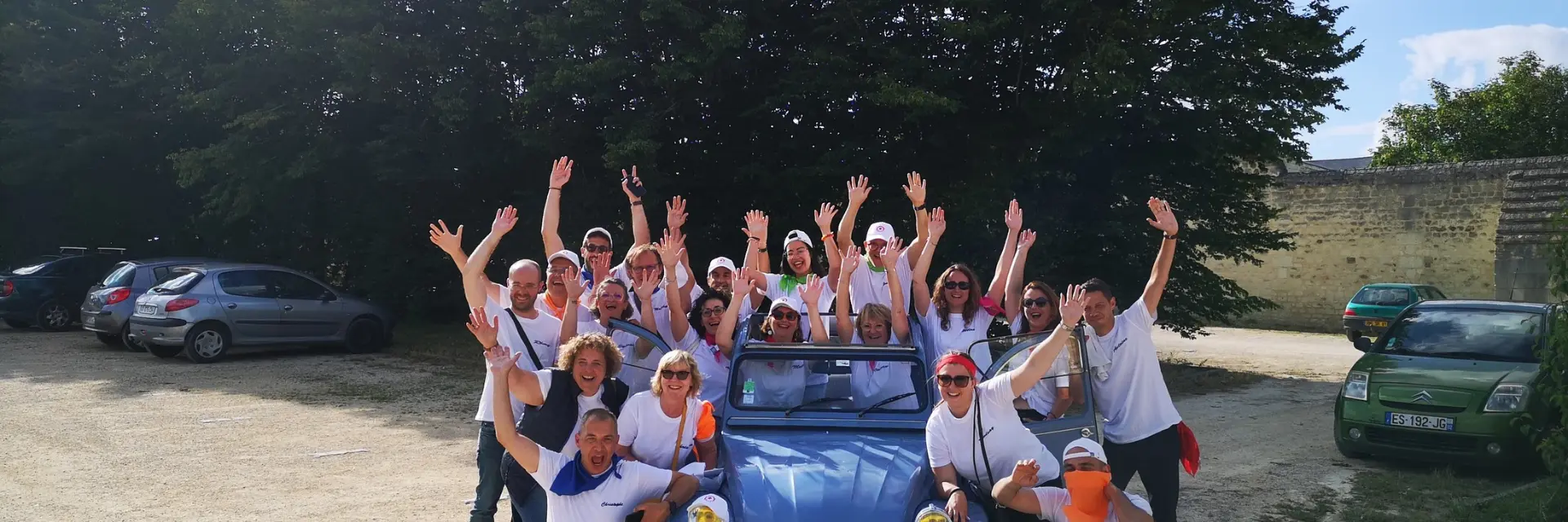 Une grande équipe de professionnels pose joyeusement autour d'une Citroën 2CV bleue