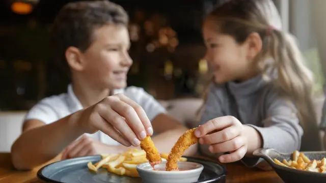 Deux enfants assis à table en train de partager un plat de frites et de beignets