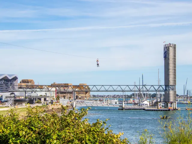 Une personne descend en tyrolienne au-dessus de l'eau face à la Cité de la Voile Éric Tabarly à Lorient