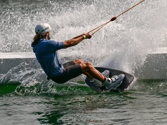 Un homme équipé d'un casque pratique le wakeboard en étant tracté sur un plan d'eau