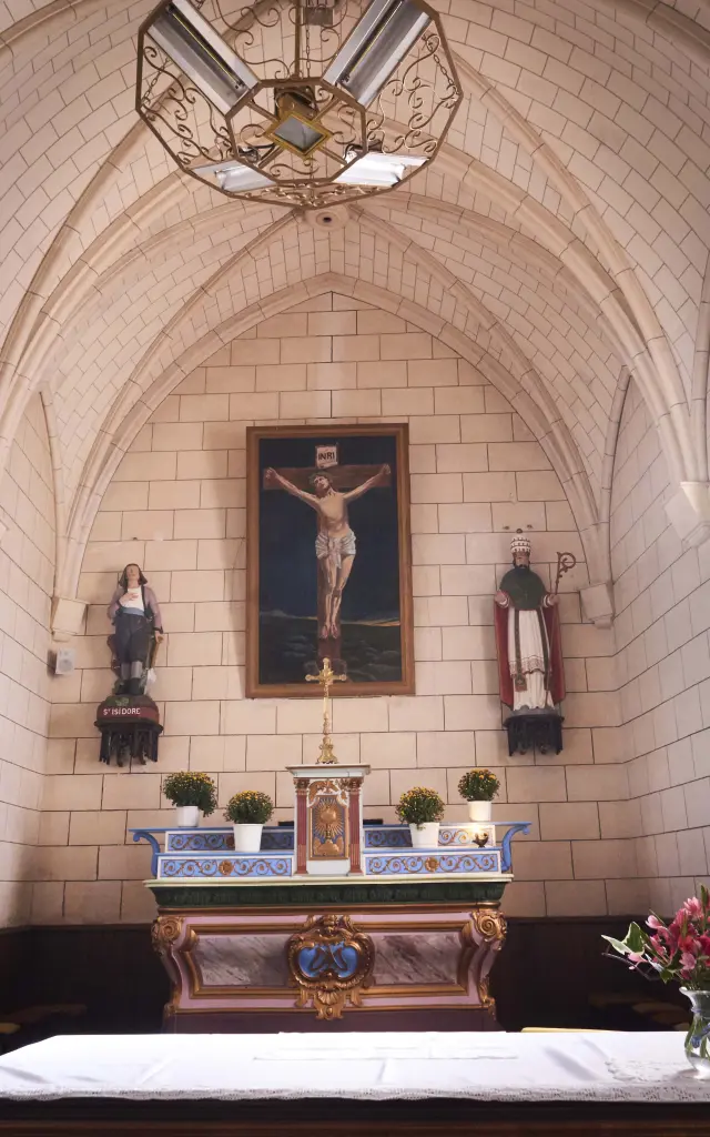 Vue intérieure du chœur d'une chapelle en pierre avec son autel, un crucifix et des vitraux