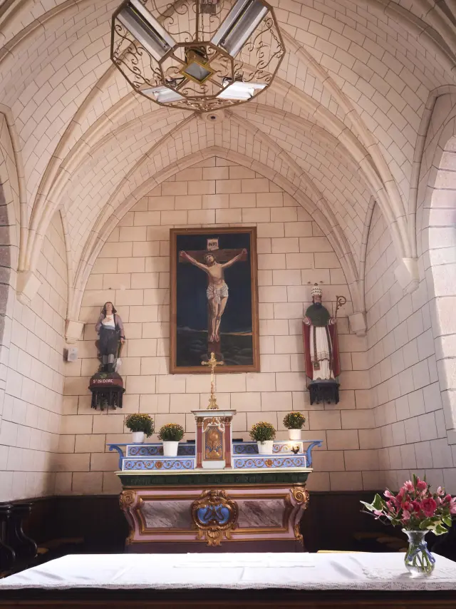 Vue intérieure du chœur d'une chapelle en pierre avec son autel, un crucifix et des vitraux