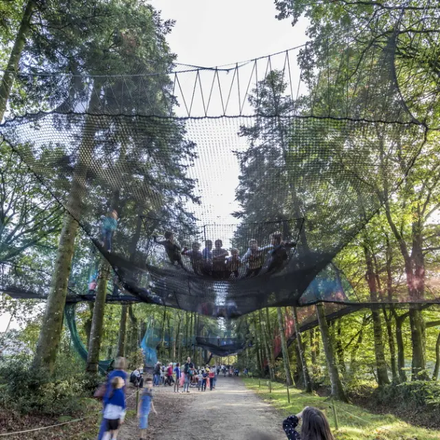 Des enfants et des visiteurs s'amusent dans de grands filets noirs de Parcabout suspendus entre les arbres du parc animalier et botanique de Branféré