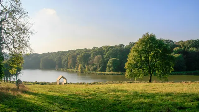 Une structure moderne en forme de silhouette de maison posée dans une prairie verdoyante au bord de l'étang du Domaine de Kerguéhennec