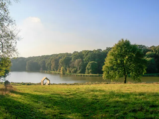Une structure moderne en forme de silhouette de maison posée dans une prairie verdoyante au bord de l'étang du Domaine de Kerguéhennec
