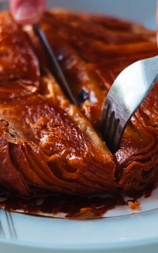 Gros plan sur un kouign-amann doré et caramélisé, découpé à l'aide d'un couteau et d'une fourchette dans une assiette