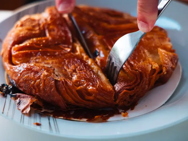 Gros plan sur un kouign-amann doré et caramélisé, découpé à l'aide d'un couteau et d'une fourchette dans une assiette