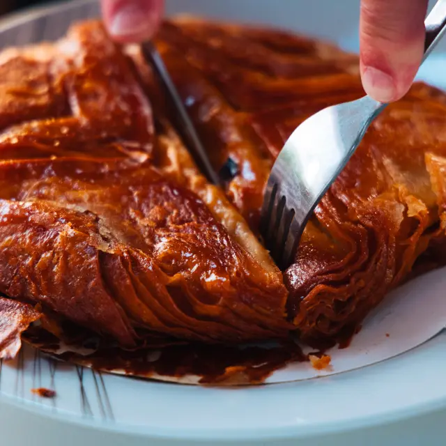 Gros plan sur un kouign-amann doré et caramélisé, découpé à l'aide d'un couteau et d'une fourchette dans une assiette