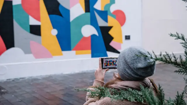 Cette photo représente une femme prenant une photo d'un mur peint avec son téléphone portable, en hiver, en ville.