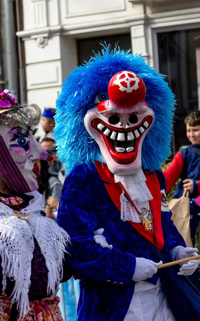 Des personnes déguisées pour le Carnaval de Mulhouse pendant la cavalcade. Les personnes portent des masques et la foule lance des confettis.