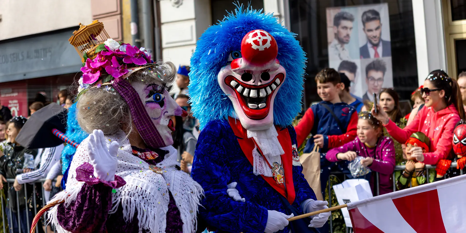 Des personnes déguisées pour le Carnaval de Mulhouse pendant la cavalcade. Les personnes portent des masques et la foule lance des confettis.
