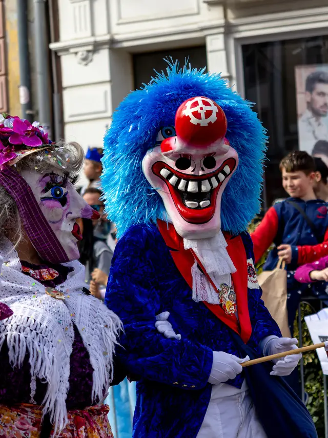 Des personnes déguisées pour le Carnaval de Mulhouse pendant la cavalcade. Les personnes portent des masques et la foule lance des confettis.