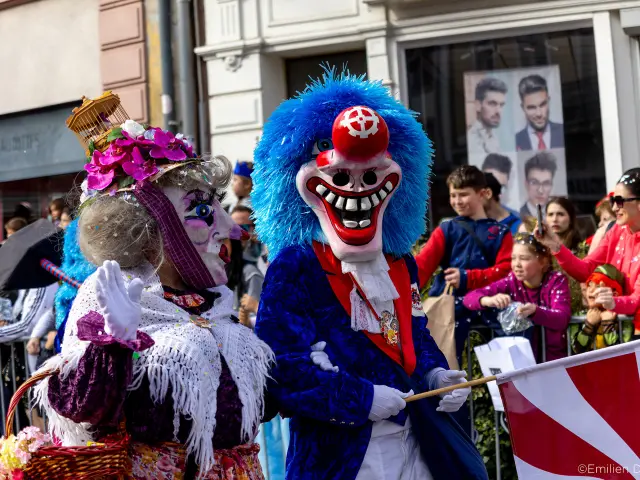 Des personnes déguisées pour le Carnaval de Mulhouse pendant la cavalcade. Les personnes portent des masques et la foule lance des confettis.
