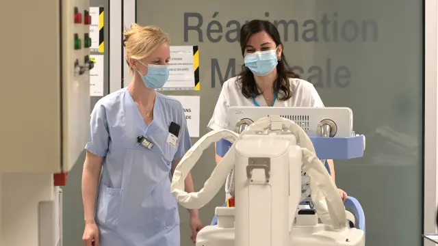 Deux infirmières masquées poussant un chariot médical dans un hôpital.