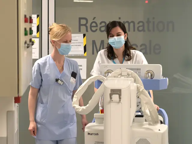 Deux infirmières masquées poussant un chariot médical dans un hôpital.