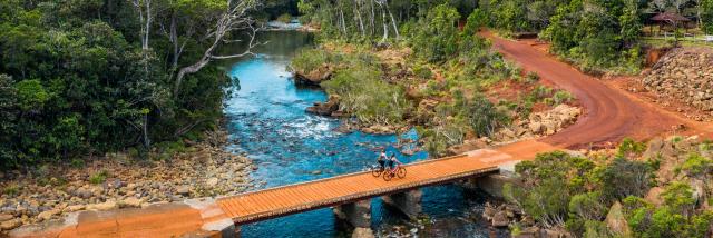 Traversée d'un pont en VTT au Parc Provincial de la Rivière Bleue à Yaté, dans le Grand Sud de la Nouvelle-Calédonie.
