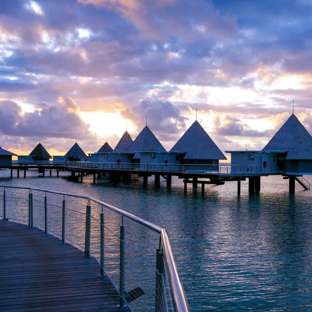 Le coucher du soleil derrière les bungalows sur pilotis de l'hôtel DoubleTree by Hilton Îlot Maître Resort à Nouméa en Nouvelle-Calédonie.