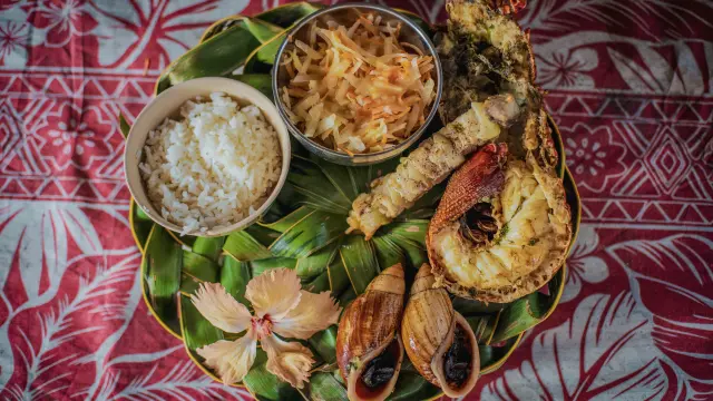 Déguster un repas calédonien : bulimes, langouste et poisson grillées accompagnés de riz et d'une salade.