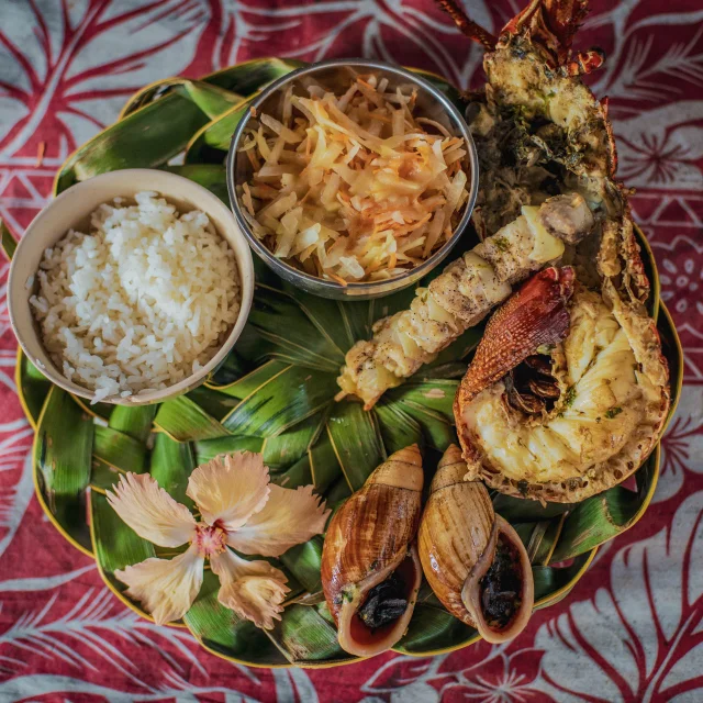 Déguster un repas calédonien : bulimes, langouste et poisson grillées accompagnés de riz et d'une salade.