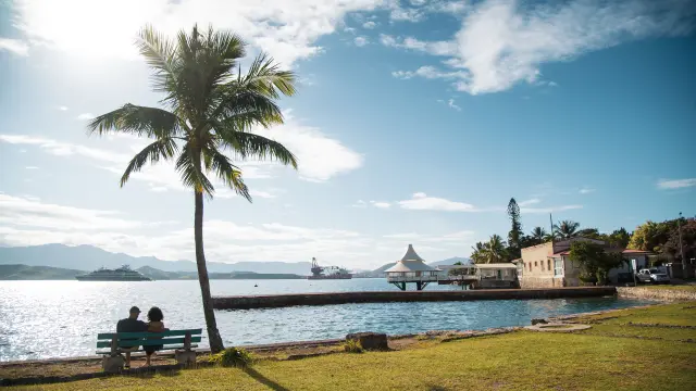 Personnes assises sur un banc face à la mer à Nouville, près d’un bâtiment historique du bagne (CREIPAC) à Nouméa.
