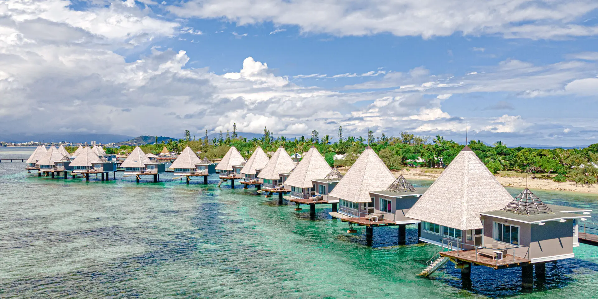 Aerial view of the DoubleTree by Hilton Nouméa overwater bungalows above a turquoise lagoon.