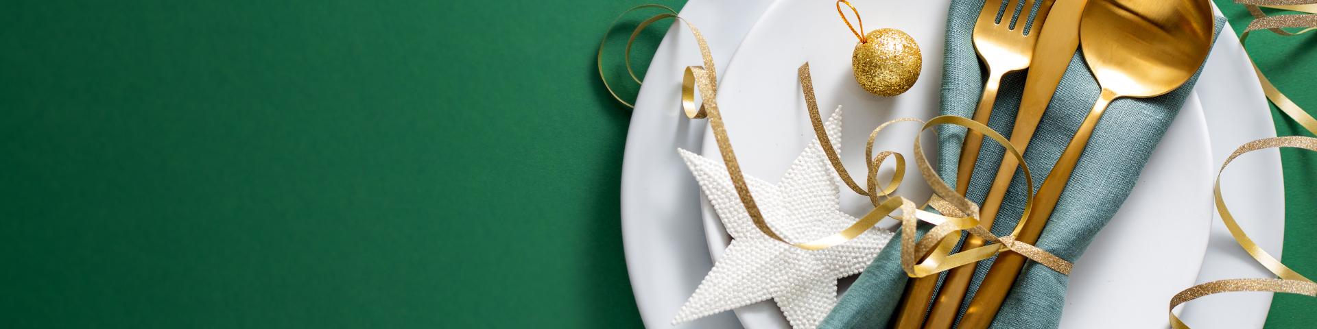 Christmas Flat Lay Background. Gold Cutlery with Bubbles served on napkin on plate on Green Background. Minimalistic design. Copy Space. Horizontal. Christmas concept.